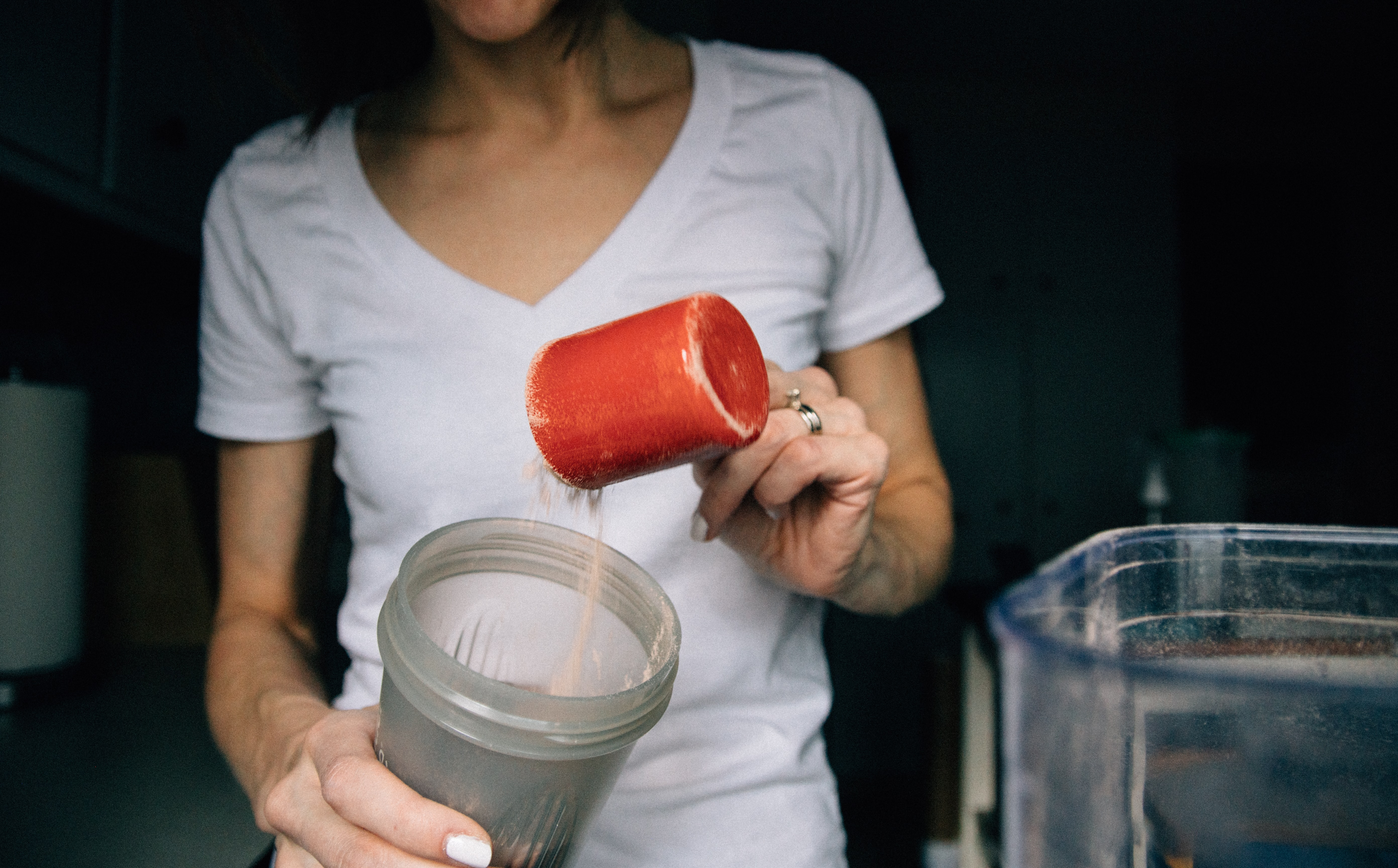 Woman pours protein powder into a blender.