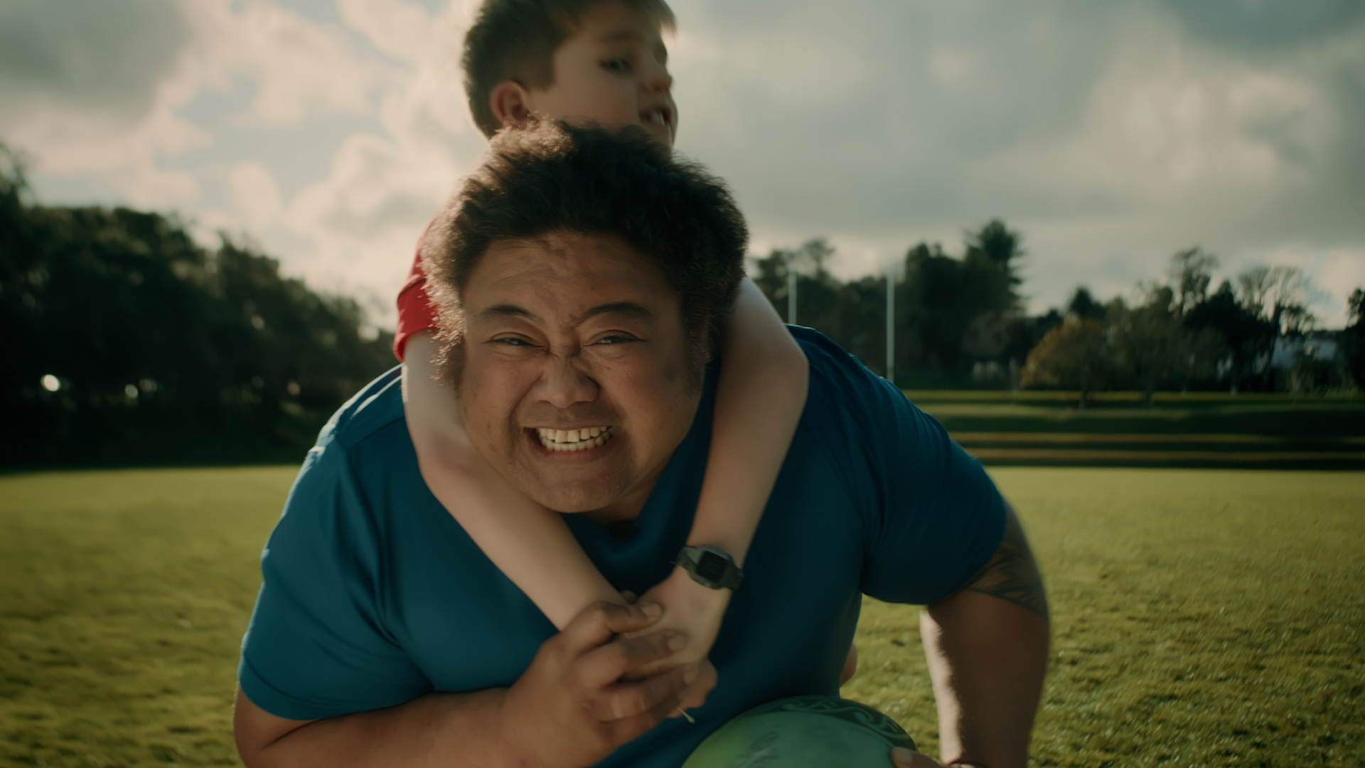 A man struggles to score a rugby try as a kid clings to his neck