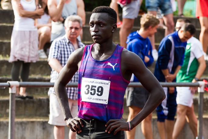 Peter Bol stands on an athletics track with a crowd behind him
